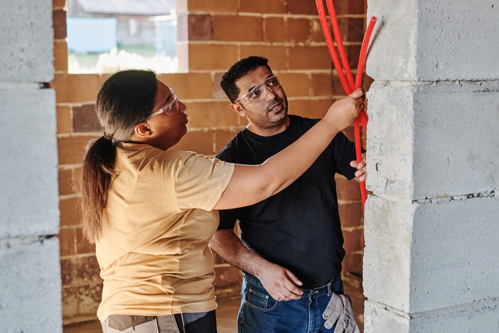 Two workers in safety goggles holding pipes